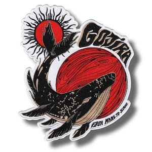 以下が含まれることがあります： 黒いクジラのデザイン、赤い太陽、そして「GOJIRA」の文字が刺繍されたパッチ。パッチには「FROM MARS TO SURFS」の文字も含まれています。クジラには星座模様があります。デザインは白い背景にあります。