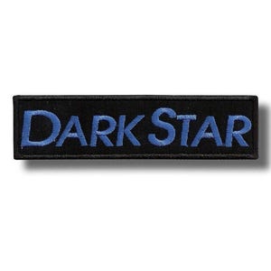 Könnte beinhalten: Ein rechteckiger, schwarzer Aufnäher mit den in blauer Farbe gestickten Worten "DARK STAR". Der Aufnäher hat einen schwarzen Rand und ist zum Aufnähen oder Aufbügeln auf Kleidung oder Accessoires gedacht.