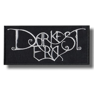 以下が含まれることがあります： 黒い長方形のパッチ。白い刺繍で「Darkest Era」の文字が施されています。パッチには白い縁取りがあり、衣服やアクセサリーに縫い付けるようにデザインされているようです。テキストが主な特徴です。