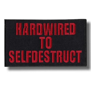以下が含まれることがあります： 「HARDWIRED TO SELFDESTRUCT」の赤い文字が刺繍された黒い長方形のパッチ。パッチは質感があり、影の効果があります。