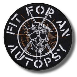 Può includere: Toppa rotonda nera con testo ricamato bianco e grafica centrale. Il testo recita "FIT FOR AN AUTOPSY" attorno al bordo. La grafica presenta un teschio con una corona di spine e linee radianti.