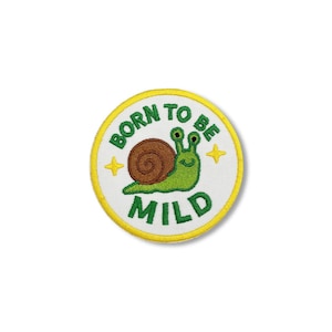 Op de afbeelding: Een ronde patch met een gele rand en een witte binnenkant. De patch toont een groene slak met een bruin huisje en de woorden "BORN TO BE MILD" in het groen. Twee gele sterren staan aan weerszijden van de slak.