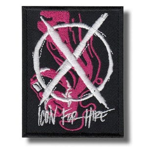 May include: Black embroidered patch featuring a pink design within a white circle and a white X. The text "ICON FOR HIRE" is embroidered in white below the design. The patch is rectangular.
