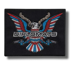 Puede incluir: Parche bordado negro con un águila estilizada con alas rojas, blancas y azules, sosteniendo dos pistolas. La palabra "DIPLOMATS" está bordada en blanco, con "HARLEM WORLD WIDE" en pancartas arriba.