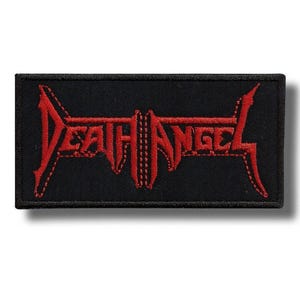 Op de afbeelding: Zwart rechthoekig embleem met de rode tekst "DEATH ANGEL" in een gestileerd, gekarteld lettertype. Het embleem heeft een rode rand en is waarschijnlijk gemaakt van stof, geschikt om op kleding of accessoires te naaien of te strijken.