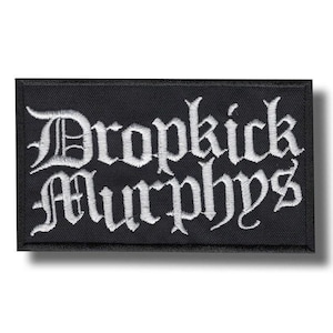 Peut inclure: Écusson rectangulaire noir avec le texte brodé "Dropkick Murphys" en lettres gothiques blanches. L'écusson a une bordure noire et est probablement conçu pour être cousu sur des vêtements ou des accessoires.