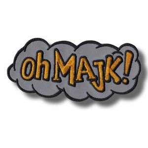 Könnte beinhalten: Gestickter Aufnäher mit dem Schriftzug "oh MAJK!" in goldfarbenen Buchstaben mit schwarzen Umrissen, vor einem grauen, wolkenförmigen Hintergrund. Der Aufnäher hat einen schwarzen Rand und ein cartoonartiges Design.