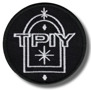 Könnte beinhalten: Ein runder, schwarzer, gestickter Aufnäher mit weißen Details. Das Design zeigt die Buchstaben "TPY" in einer geometrischen Form, ergänzt durch Stern- und Punktmuster. Geeignet für Kleidung oder Accessoires.