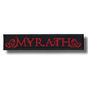 Puede incluir: Parche rectangular negro con la palabra "MYRATH" bordada en rojo, con adornos decorativos en cada extremo. Adecuado para ropa o accesorios.
