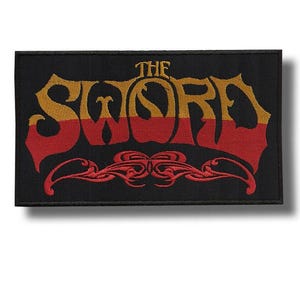 Può includere: Toppa rettangolare nera con la scritta "THE SWORD" ricamata in oro e rosso. Il design presenta un carattere stilizzato ed elementi decorativi, adatta per giacche o borse.