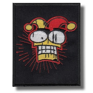 Może przedstawiać: Haftowana naszywka z twarzą kreskówkowego błazna. Projekt przedstawia żółtą głowę, białe oczy oraz czerwono-żółty kapelusz. Twarz ma szeroki uśmiech, na czarnym tle z czerwonymi liniami.
