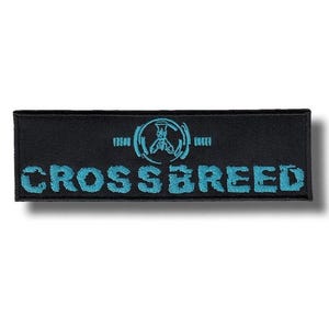 Könnte beinhalten: Schwarzer rechteckiger Aufnäher mit dem Wort "CROSSBREED" in Türkis, unter einem türkisfarbenen Emblem. Das Emblem ist ein stilisiertes Design in einem Kreis. Geeignet für Kleidung oder Accessoires.
