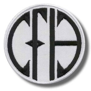 Puede incluir: Un parche bordado circular con fondo blanco y diseño negro. El diseño presenta un monograma o emblema estilizado dentro de un borde ovalado negro. El emblema incluye líneas verticales y horizontales y formas de flecha.