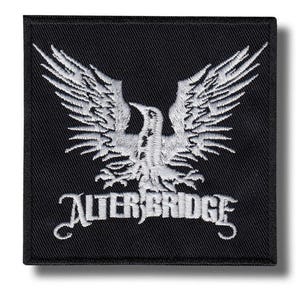 Può includere: Toppa quadrata nera con un disegno di aquila ricamata in bianco e il nome della band "ALTER BRIDGE" in corsivo bianco. L'aquila ha le ali spiegate e la toppa ha un bordo nero.