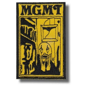 Op de afbeelding: Een rechthoekige patch met het woord "MGMT" in vette, zwarte letters bovenaan. De patch heeft een gele achtergrond met een zwarte illustratie van een trieste clown en architecturale elementen.