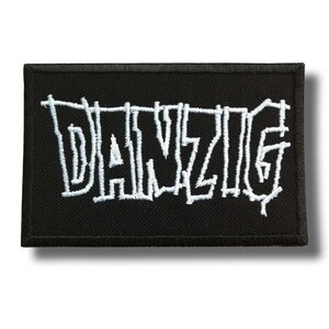 Może przedstawiać: Czarna prostokątna naszywka z białym haftowanym napisem "DANZIG". Naszywka ma czarną obwódkę i białą haftowaną czcionkę. Naszywka jest prawdopodobnie przeznaczona na kurtkę lub torbę.