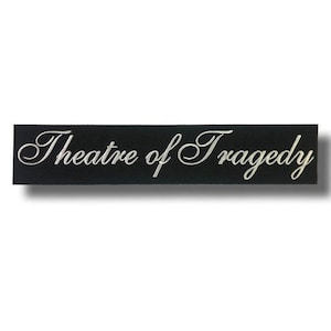 Könnte beinhalten: Ein schwarzes, rechteckiges Schild mit dem Schriftzug "Theatre of Tragedy" in weißer, geschwungener Schrift. Der Schriftzug ist elegant. Ein leichter Schatten deutet auf eine Erhebung hin.