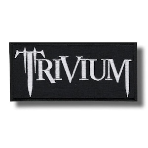 May include: Black rectangular patch with the word "TRIVIUM" embroidered in white, stylized lettering. The patch has a black border and is likely for clothing or accessories.