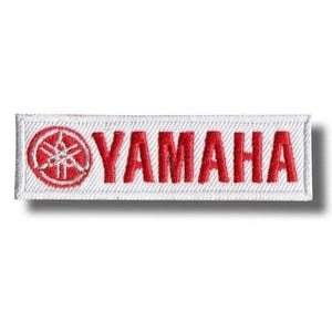 Puede incluir: Parche bordado de Yamaha con el logotipo de Yamaha en rojo sobre un fondo rectangular blanco. El logotipo incluye un emblema rojo y el nombre de la marca en negrita y mayúsculas.