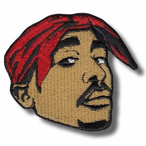 May include: Embroidered patch featuring a portrait of a man with a red bandana and a goatee. The patch has a tan face, black eyebrows, and a black mustache. The patch is an oval shape.