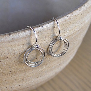 May include: A pair of silver dangle earrings with three interlocking circles. The earrings have a small bead at the top of the dangle.