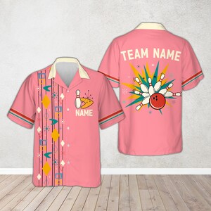 Pode incluir: Camisa de boliche rosa com gola creme e mangas curtas. A frente apresenta um gráfico de pino de boliche e a palavra "NAME". A parte de trás mostra uma bola de boliche atingindo pinos com as palavras "TEAM NAME".