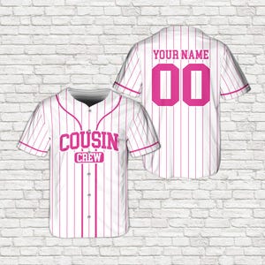 May include: White baseball jersey with pink vertical stripes and accents. The front of the jersey displays the text "COUSIN CREW" in pink. The back of the jersey has the text "YOUR NAME" above the number "00" in pink.