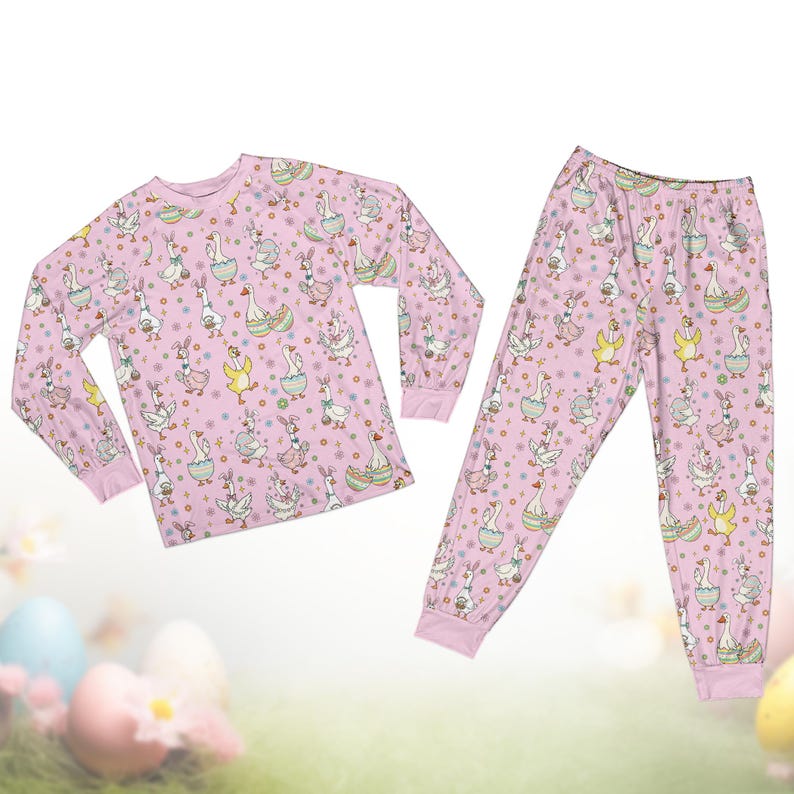 Op de afbeelding: Een lichtroze pyjamaset met een herhaald patroon van ganzen, konijnen en paaseieren. De top met lange mouwen en de broek hebben roze manchetten. De ganzen staan in verschillende poses, sommige dragen mutsen en houden manden vast.