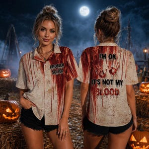 May include: A short-sleeve button-down shirt featuring a beige base with a red blood splatter pattern. The front displays the text "PROBLEM SOLVED" and the back features two red handprints with the text "I'M OK IT'S NOT MY BLOOD" in black.