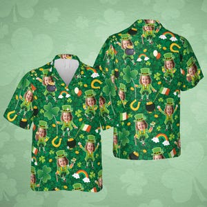 May include: Green button-down shirt with a St. Patrick's Day theme. The shirt features a repeating pattern of a child dressed as a leprechaun, rainbows, shamrocks, horseshoes, and pots of gold. The shirt has a white collar.
