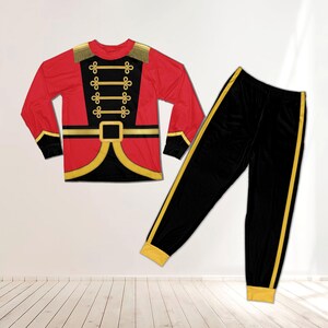 May include: A two-piece pajama set featuring a long-sleeve red shirt with gold trim, epaulets, and a black front panel with gold braided details resembling a uniform. The matching black pants have a gold stripe down each side and gold cuffs.