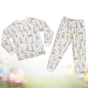 Op de afbeelding: Witte pyjamaset met een herhaald patroon van ganzen, konijnen en paaseieren. De top met lange mouwen en de broek hebben een grillig ontwerp met pastelkleuren en bloemaccenten, perfect voor Pasen of de lente. De pyjamaset is gemaakt van een zacht, comfortabel materiaal.