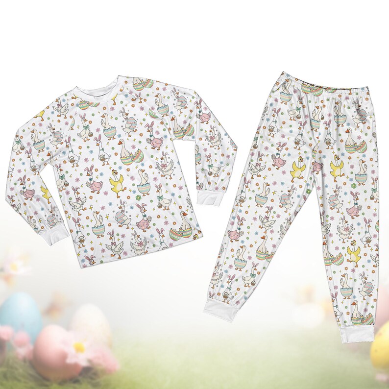Op de afbeelding: Witte pyjamaset met een herhaald patroon van ganzen, konijnen en paaseieren. De top met lange mouwen en de broek hebben een grillig ontwerp met pastelkleuren en bloemaccenten, perfect voor Pasen of de lente. De pyjamaset is gemaakt van een zacht, comfortabel materiaal.