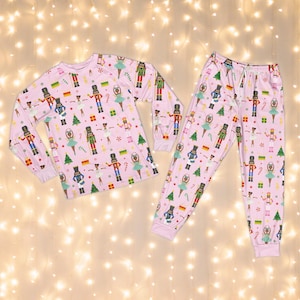 May include: Pink pajama set with a repeating pattern of nutcrackers, ballerinas, Christmas trees, and gift boxes. The long-sleeved top and pants are made of a soft material, perfect for a cozy night's sleep.