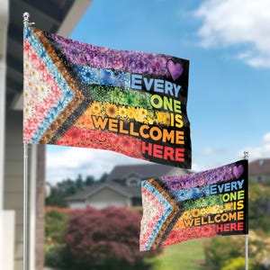 Puede incluir: Dos banderas para exteriores con un diseño floral de arcoíris y el texto "EVERYONE IS WELCOME HERE". Las banderas presentan un corazón y una variedad de flores en un patrón de arcoíris, con un fondo negro.