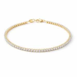 May include: A gold tennis bracelet with a row of small, clear gemstones. The bracelet is on a white background. The clasp is visible. The bracelet is a delicate piece of jewelry.