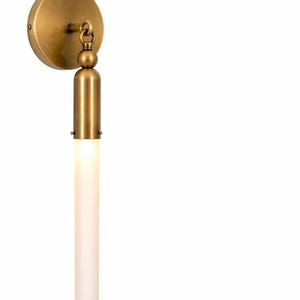 Könnte beinhalten: Messing-Wandleuchte mit kreisförmiger Rückplatte und zylindrischer Leuchte. Die Leuchte ist mattweiß und strahlt ein sanftes Licht aus. Die Leuchte hat eine Vintage-Ästhetik, ideal für die Innenbeleuchtung. Etwa 20 cm lang.