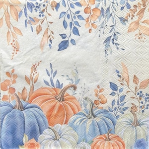 May include: A decorative paper napkin featuring a fall harvest theme. The design includes a collection of pumpkins in shades of blue, orange, and white, with brown stems. The pumpkins are surrounded by blue and brown leaves and floral accents.