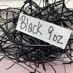 May include: A tangled mass of glossy black material. A white label displays the text "Black 9oz" in handwritten style. The image showcases a close-up view of the dark, possibly plastic, strands.