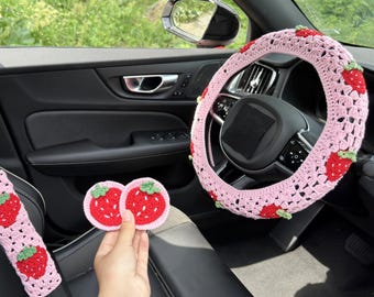 May include: Pink crochet car accessories set with red strawberry accents. Includes a steering wheel cover, seat belt covers, and two coasters. The strawberry designs have green leaves.