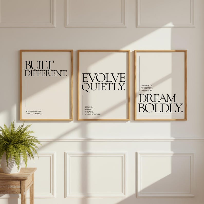 May include: Three framed art prints with inspirational quotes. The prints have a cream background and wooden frames. The quotes read "BUILT DIFFERENT," "EVOLVE QUIETLY," and "DREAM BOLDLY." The first print also says "NOT FOR EVERYONE MADE FOR PURPOSE."