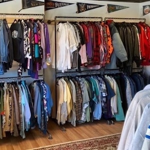 Peut inclure: Un magasin de vêtements vintage avec des portants remplis de vêtements. Les vêtements comprennent des chemises, des vestes et des pulls de différentes couleurs et motifs. Le magasin a une esthétique rustique avec des portants en tuyaux métalliques et des fanions au plafond.