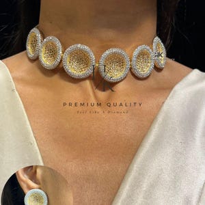 Op de afbeelding: Een goudkleurige choker ketting met cirkelvormige, getextureerde hangers, elk omlijnd met sprankelende witte stenen. De bijpassende oorbel is ook zichtbaar. De tekst "PREMIUM QUALITY" en "Feel like a Diamond" is op de afbeelding gedrukt.