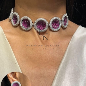 Puede incluir: Un collar gargantilla plateado con piedras magenta circulares rodeadas de cristales transparentes. También se ven pendientes a juego de color magenta y cristal. Se muestra el texto "PREMIUM QUALITY" y "Feel Like A Diamond".