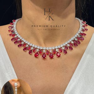 Peut inclure: Un ensemble collier et boucles d'oreilles étincelant, orné de pierres précieuses rouges en forme de goutte. Le collier est orné de pierres blanches scintillantes et du texte "PREMIUM QUALITY Feel Like A Diamond". Un bijou magnifique.
