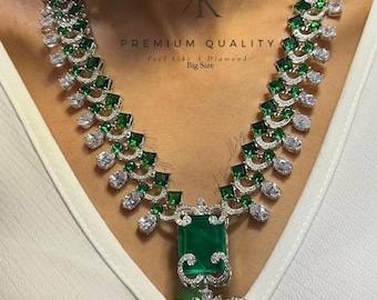 May include: A luxurious necklace featuring emerald-cut green gemstones and sparkling white stones. The necklace has a large pendant with a central emerald and intricate detailing. The words "PREMIUM QUALITY" and "Big Size" are visible.