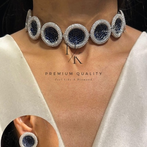 Op de afbeelding: Een choker ketting en bijpassende oorbel set. De ketting en oorbellen hebben ovale elementen met een donkerblauw centrum omringd door heldere stenen. De tekst "PREMIUM QUALITY" en "feel like a Diamond" is zichtbaar.