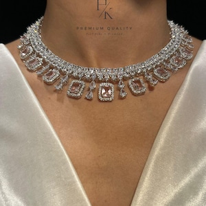 Peut inclure: Un collier argenté étincelant orné de pierres roses carrées et rectangulaires, ainsi que de petites pierres transparentes. Le collier est mis en valeur sur un fond blanc, avec le texte "HK PREMIUM QUALITY Feel like a Diamond".