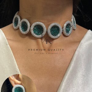 Op de afbeelding: Een choker ketting en bijpassende oorbel set. De ketting heeft een reeks cirkelvormige smaragdgroene stenen omgeven door een halo van heldere kristallen. De oorbel weerspiegelt het kettingontwerp. De tekst "PREMIUM QUALITY" en "Feel Like A Diamond" is zichtbaar.