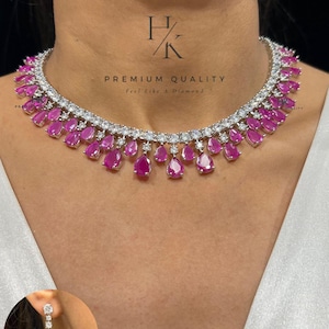 May include: A silver necklace featuring clear stones and pink, teardrop-shaped gems. The necklace is worn around a person's neck. A matching earring is also shown. The text "PREMIUM QUALITY" is visible in the image.